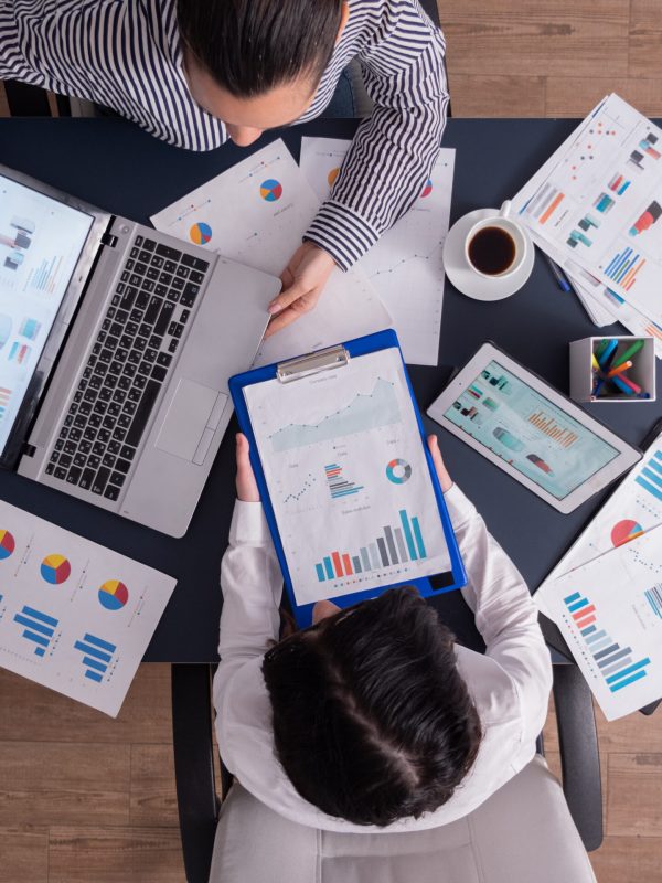 Top viewTop view of manager and employee doing teamwork in business office , looking at charts on laptop display. Finance paperwork with charts at workplace. Discusing financial plan.